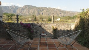 Un patio con dos sillas de metal y una mesita, con vistas a un paisaje montañoso.
