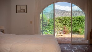 Un dormitorio con una cama grande, un cuadro en la pared y vistas a un jardín a través de un ventanal.