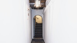 A narrow hallway with a wooden staircase leading to an archway.