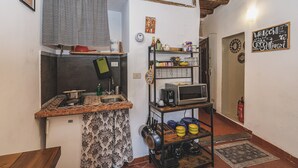 A compact kitchen with a tiled backsplash, a small sink, and a microwave on a shelf.