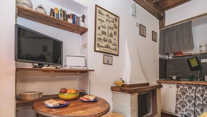 A cozy kitchen with a dining table, a fireplace, and a bookshelf with books and decorative items.