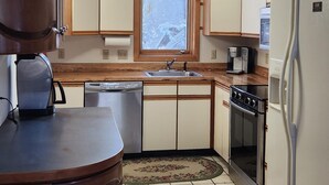 A compact kitchen with wooden cabinets, a built-in dishwasher, a stove, and a refrigerator. - Peaceful, Sunlit Condo on Haystack Golf Course (Wilmington)