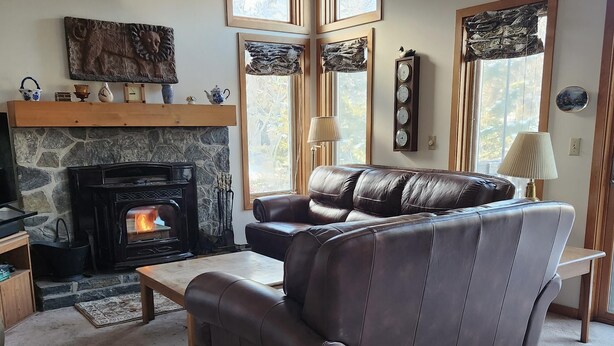 A cozy living room with a stone fireplace, leather sofa, and a television. - Peaceful, Sunlit Condo on Haystack Golf Course (Wilmington)