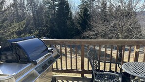 A deck with a stainless steel grill, a metal table, and chairs. - Peaceful, Sunlit Condo on Haystack Golf Course (Wilmington)