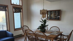 A dining area with a wooden table, six chairs, a potted plant, a chandelier, and a painting on the wall. - Peaceful, Sunlit Condo on Haystack Golf Course (Wilmington)