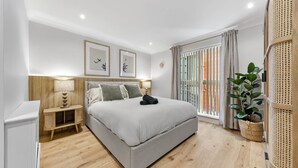 Une chambre à coucher moderne avec un grand lit, des tables de chevet, une lampe fixée au mur et une plante en pot.