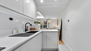 Une cuisine moderne avec des meubles blancs, un évier encastré et un petit îlot central doté d’une bouilloire.