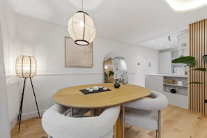 Ett modernt matområde med ett runt träbord, två grå stoppade stolar, en hängande lampa, ett inramat konstverk och en spegel på väggen.