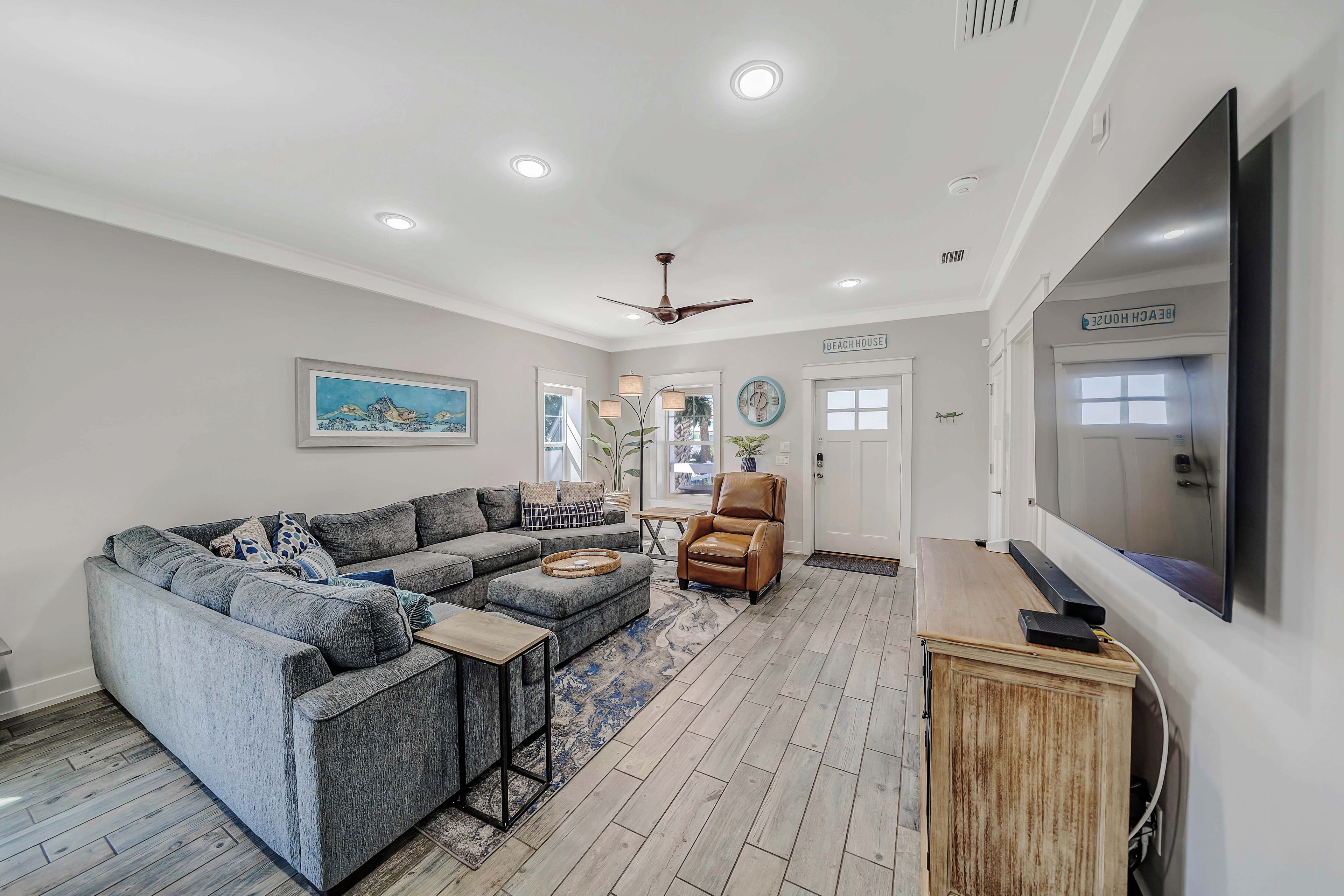 A modern living room with a sectional sofa, a leather armchair, a flat-screen TV, and a ceiling fan.