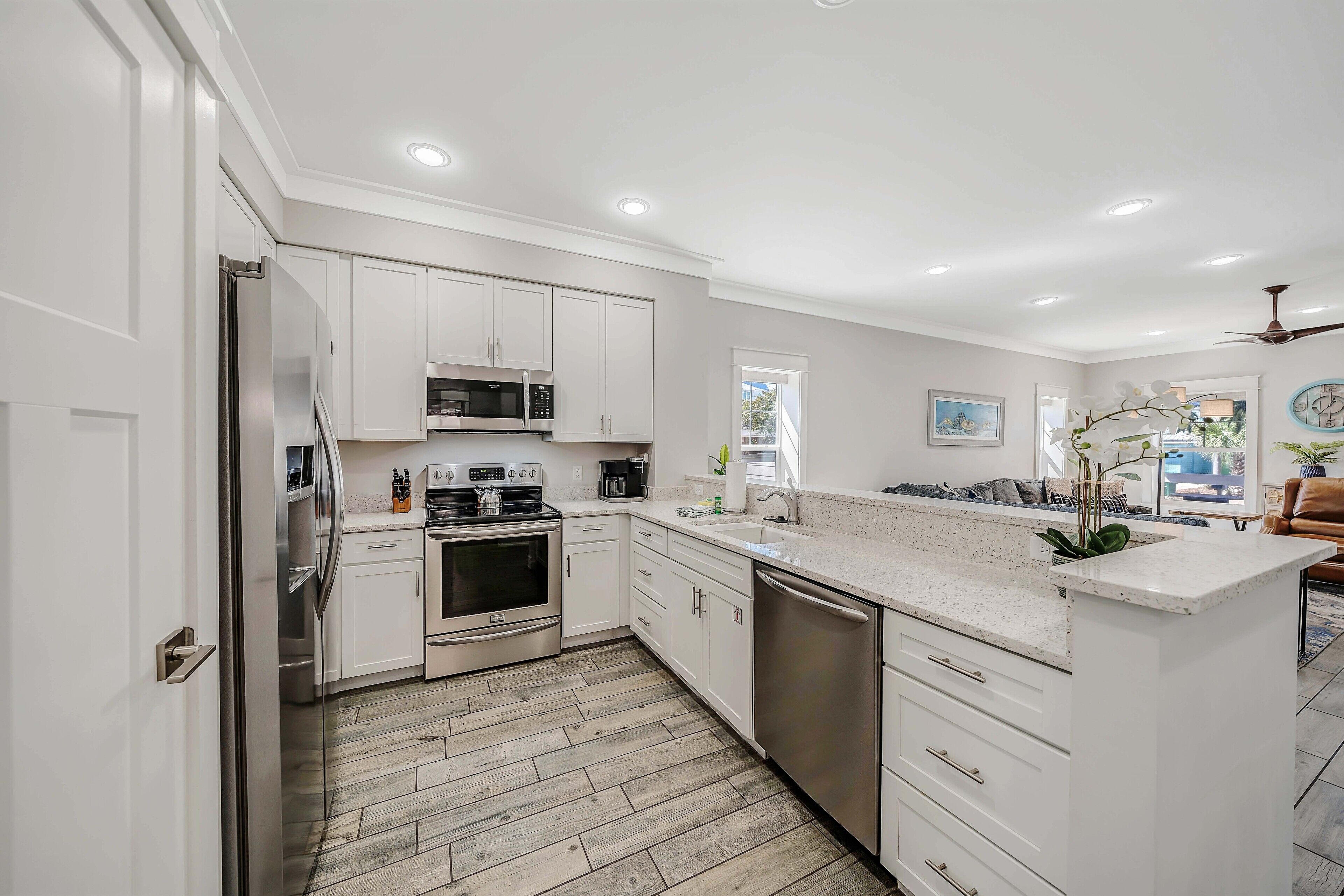A modern kitchen with white cabinetry, stainless steel appliances, and a herringbone wood floor.