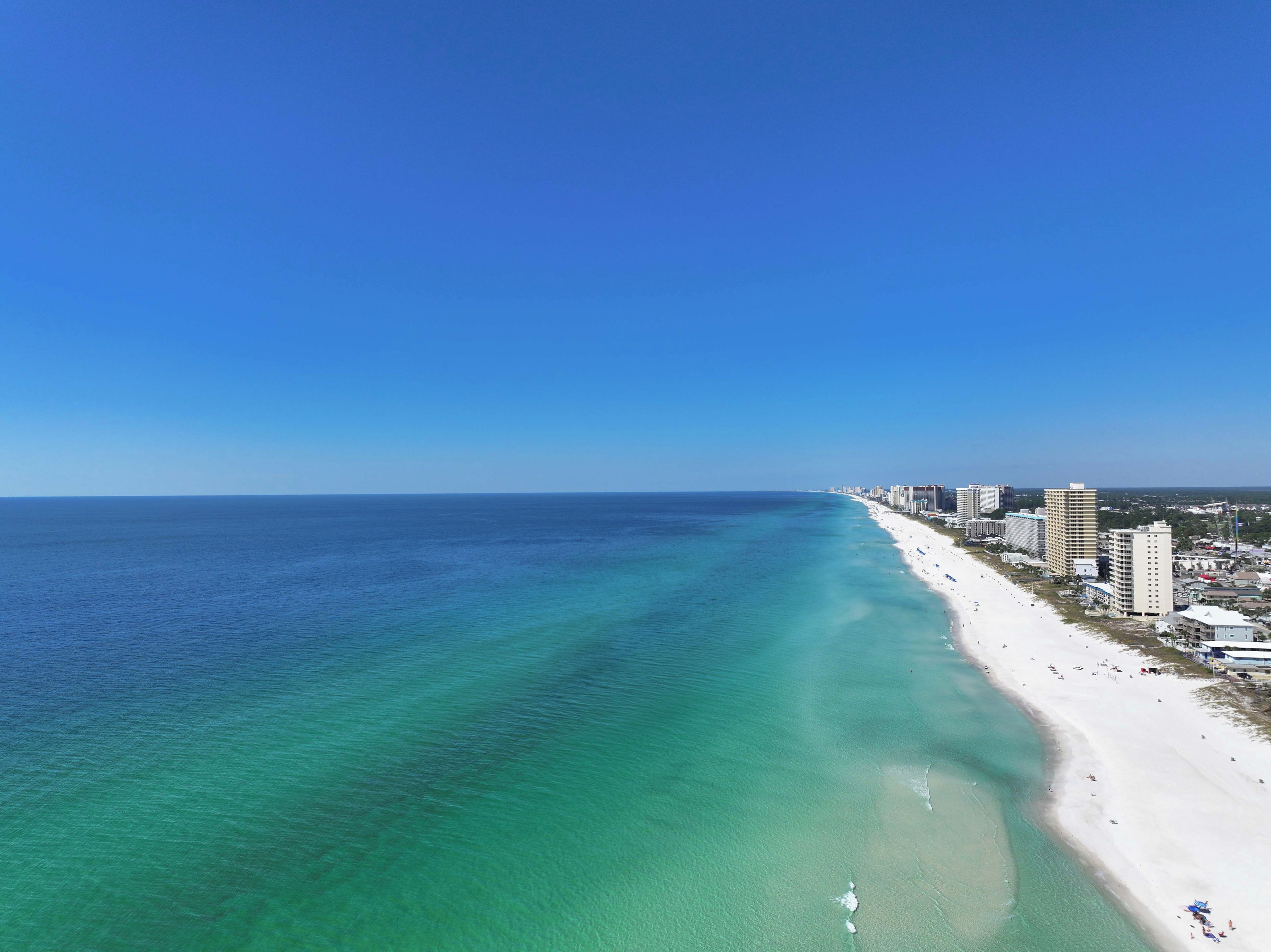 A coastal cityscape with a long sandy beach and a clear blue sky.