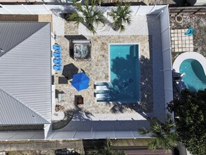 An aerial view of a backyard with a rectangular swimming pool, surrounded by a patio area with seating and umbrellas.