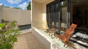 A balcony with a glass door, a wooden chair, a small stool, and potted plants. - Studio By The Pool, Jacuzzi (Tulum)