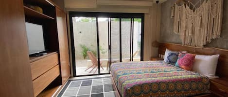 A bedroom with a bed, a ceiling fan, a TV, and a sliding glass door leading to an outdoor area.