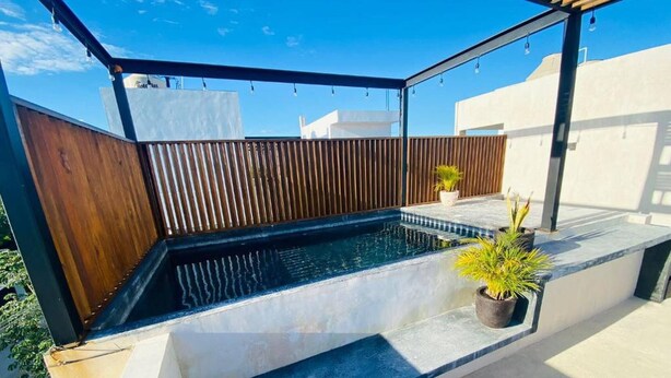 A rooftop pool area with a wooden fence, potted plants, and a clear blue sky. - Studio By The Pool, Jacuzzi (Tulum)