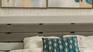 Een slaapkamer met een bed, kussens en twee abstracte schilderijen aan de muur.
