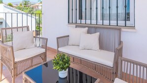 Un balcon agrémenté de meubles en osier, notamment deux chaises et un canapé, ainsi que d’une plante en pot.