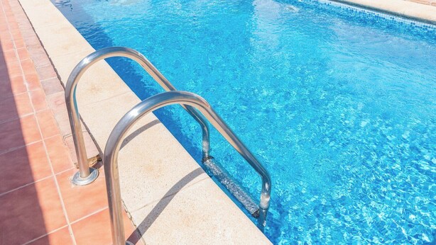 Une piscine à l’eau d’un bleu limpide, avec une échelle métallique qui y mène.