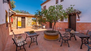 Un patio al aire libre con paredes de piedra, un macetero central con un árbol y mobiliario exterior.