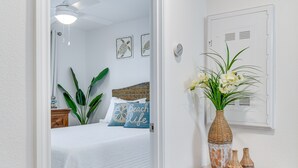 Quarto com cama, ventilador de teto, mesa de cabeceira, vaso com flores e luminária na parede.