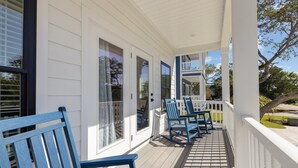 Eine überdachte Veranda mit weißen Geländern, blauen Schaukelstühlen und einer Holzterrasse.