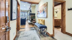 A hallway with wooden doors, a bench, a stone fireplace, and a painting on the wall. - Charlie's Slopeside: Bear Paw, Ski-In/Out, Sleeps 8, Bachelor Gulch + Ritz Pool & Hot Tub Access (Beaver Creek)