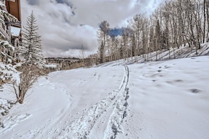 A snow-covered ski trail with footprints, a wooden building on the left, and leafless trees. - Charlie Rentz: Bear Paw, Ski-In/Out, Sleeps 8, Bachelor Gulch + Ritz Pool & Hot Tub Access (Beaver Creek)