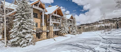 A multi-story lodge with a stone facade, wooden balconies, and snow-covered surroundings.