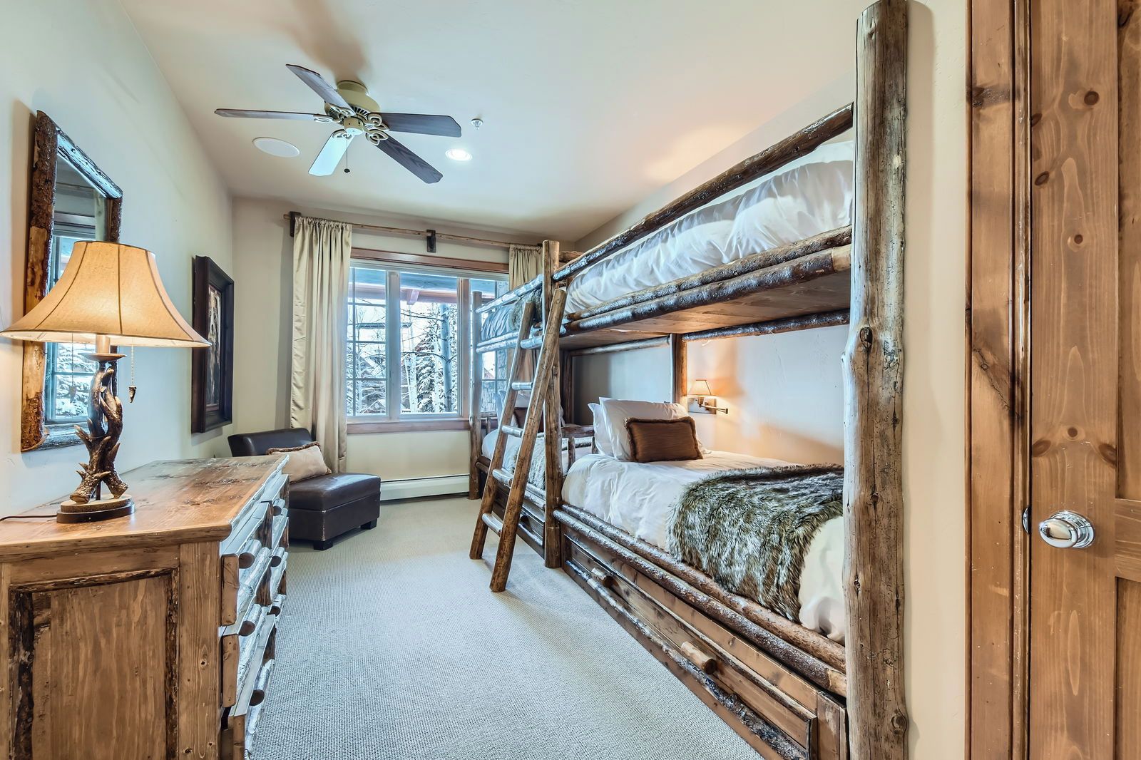A rustic room with a bunk bed, a desk with a lamp, a chair, and a ceiling fan.
