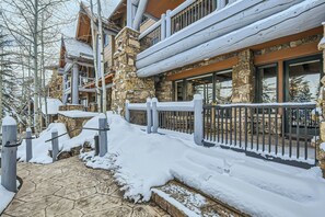 Un bâtiment en pierre recouvert de neige, doté d’une terrasse en bois et d’une rambarde en métal.