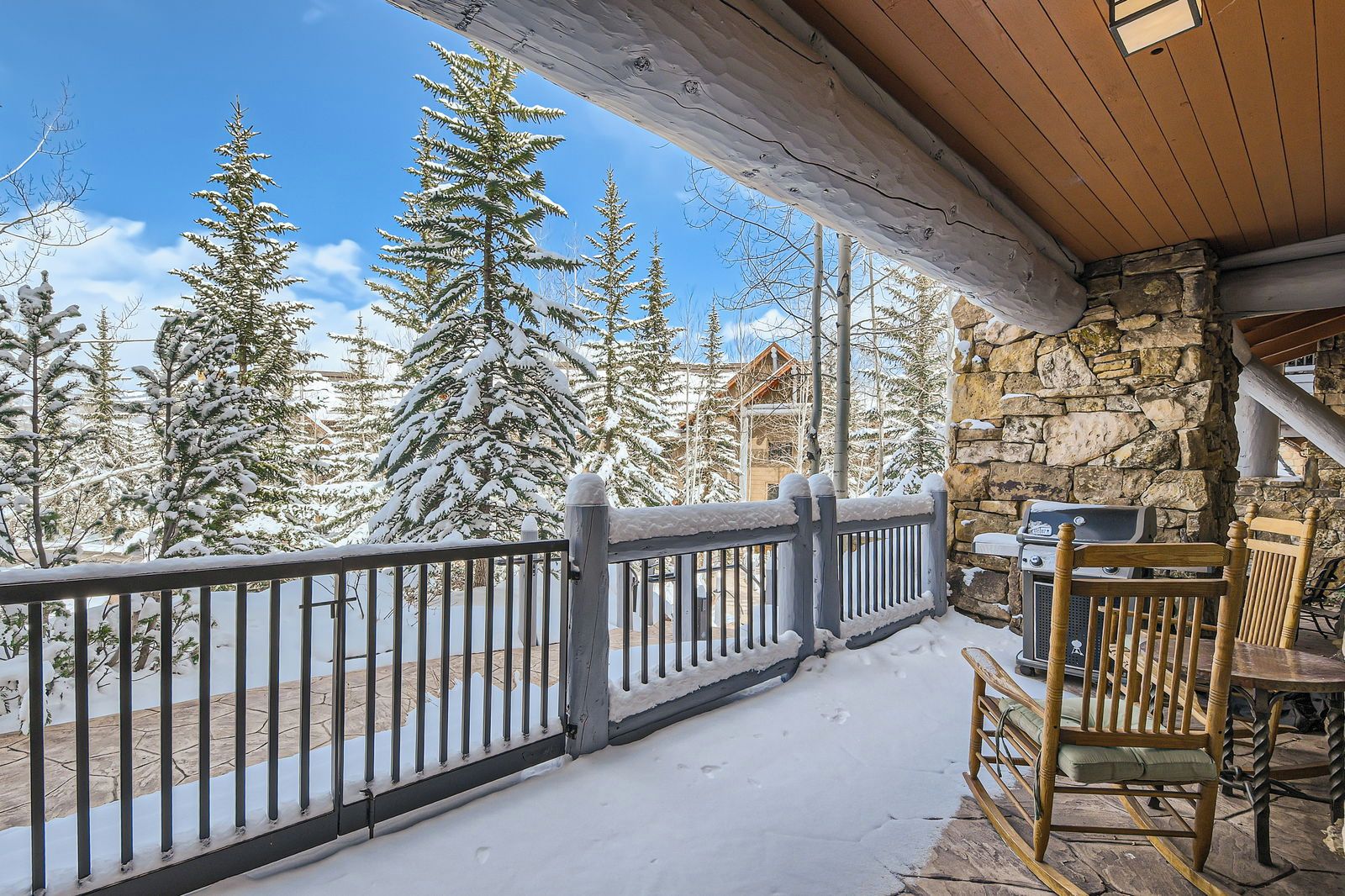 A covered outdoor area with a stone wall, a wooden railing, and a grill.