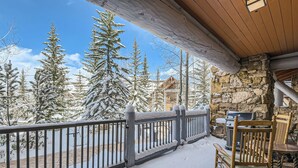 A covered outdoor area with a stone wall, a wooden railing, and a grill. - Spacious 3BR ski-in/out Beaver Creek condo with valley views. (Beaver Creek)