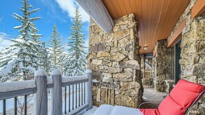 A stone exterior wall, a wooden deck, and a red chair with a snow-covered cushion. - Charlie's Slopeside: Bear Paw, Ski-In/Out, Sleeps 8, Bachelor Gulch + Ritz Pool & Hot Tub Access (Beaver Creek)