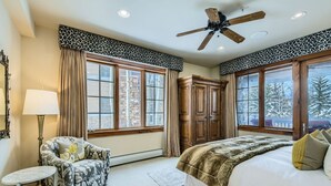 A bedroom with a large bed, a ceiling fan, a wooden wardrobe, and a window with a view of trees. - Spacious 3BR ski-in/out Beaver Creek condo with valley views. (Beaver Creek)