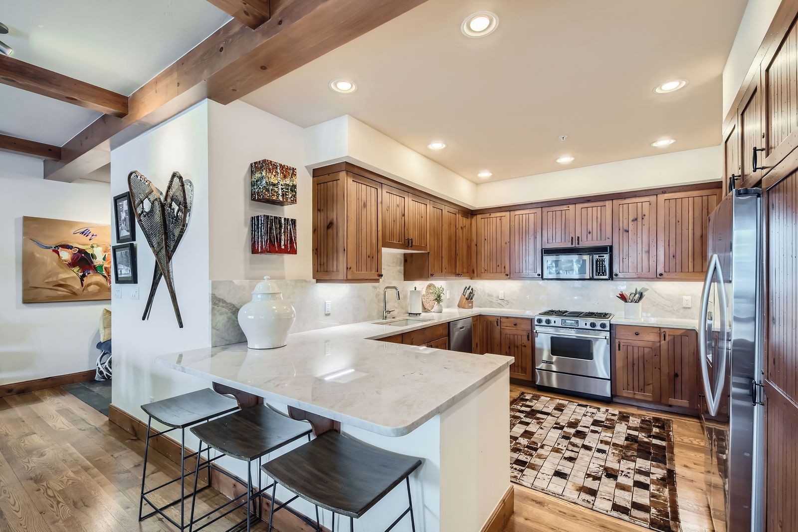 Une cuisine moderne avec des meubles en bois, un grand îlot central doté de tabourets, des appareils électroménagers en acier inoxydable et un tapis décoratif.