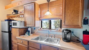 A kitchen with wooden cabinets, a stainless steel refrigerator, a double sink, and a coffee maker. - TreeHouse on Rainbow (Big Bear City)