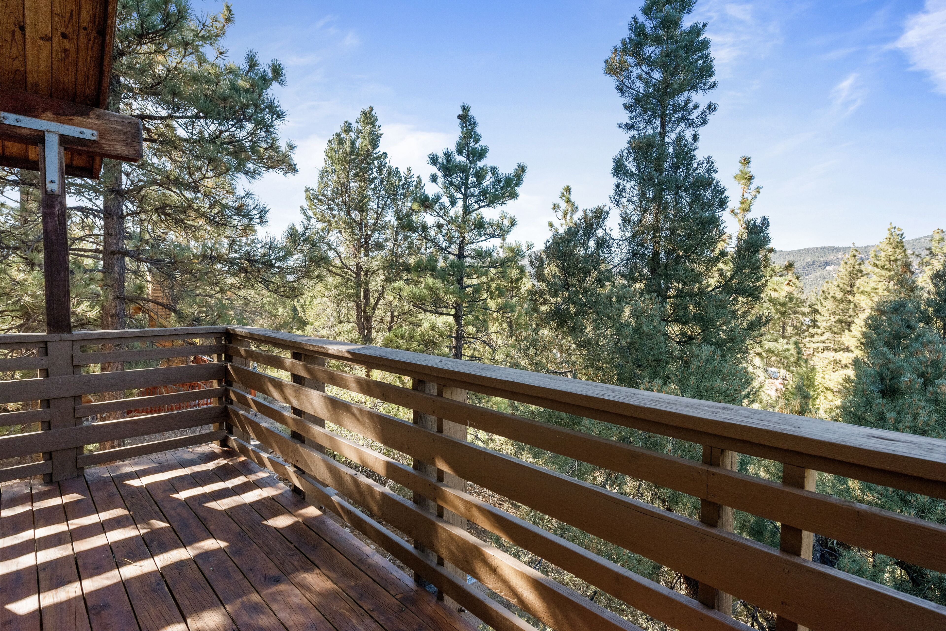 A wooden deck with a railing overlooking a forested area.