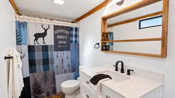 A bathroom with a shower curtain featuring a deer and trees, a white toilet, a sink with a mirror, and a towel rack.