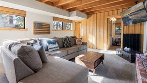 A cozy living room with a sectional sofa, a wooden coffee table, and a fireplace. - TreeHouse on Rainbow (Big Bear City)