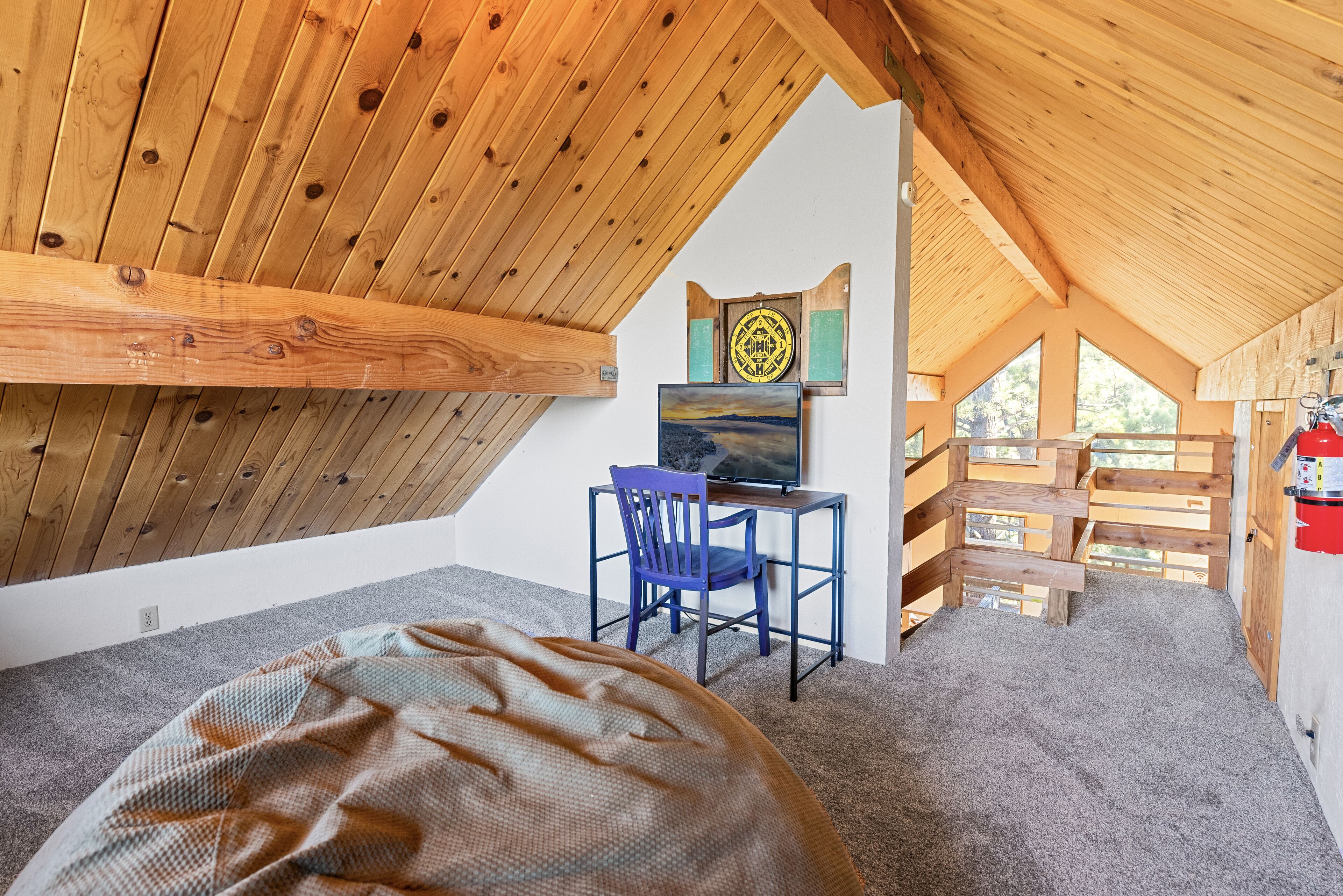 Une pièce mansardée chaleureuse avec un plafond en bois, un bureau avec une chaise et un tableau accroché au mur.