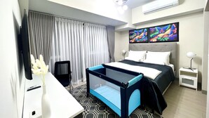 Ein modernes Hotelzimmer mit Bett, Schreibtisch, Sessel, Fernseher und einem Fenster mit Vorhängen.