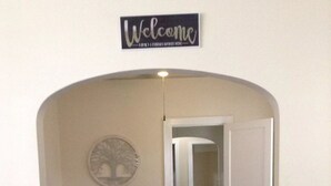 Un coin repas avec une table dressée pour quatre personnes, une pancarte « Bienvenue » au-dessus, et une porte donnant sur une autre pièce.
