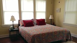 Une chambre avec un grand lit, deux tables de chevet et trois fenêtres.