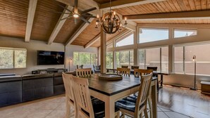 A spacious dining area with a high ceiling, large windows, and a chandelier.