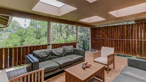 A covered patio with a sofa, chairs, and a table, featuring skylights and a view of greenery.