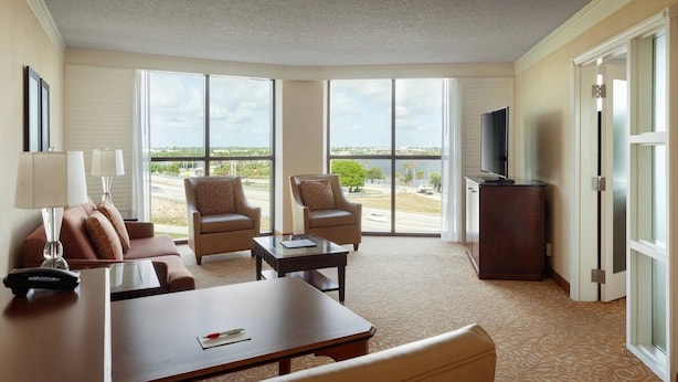 A hotel room with a large window, a flat-screen TV, a sofa, two armchairs, a coffee table, and a desk. - Welcome to The Courtyard at The Villages!
A Cozy Floridian Escape. All Luxuries! (Wildwood)