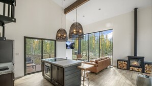 A modern kitchen with a central island, a dining area with a wooden table, a sofa, and a fireplace. - Off Grid Stays - Treehouse #3 (Columbia Falls)