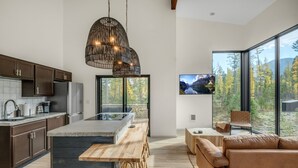 A modern kitchen with a large island, dark wooden cabinets, and a hanging light fixture. - Off Grid Stays - Treehouse #3 (Columbia Falls)