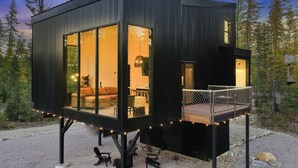 A modern cabin with large windows, a deck, and a cozy interior. - Off Grid Stays - Treehouse #3 (Columbia Falls)
