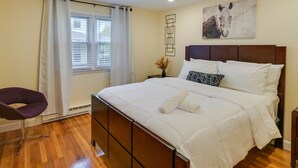 Un dormitorio con cama, una silla, un ventanal con cortinas y una obra de arte en la pared.